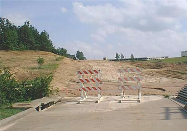 Historical photo showing Silver Springs Road under construction in the 1990s, with barricades blocking a newly poured roadway, exposed dirt and grading, and the view looking south from Independence Street toward William Street and Saint Francis Medical Center.